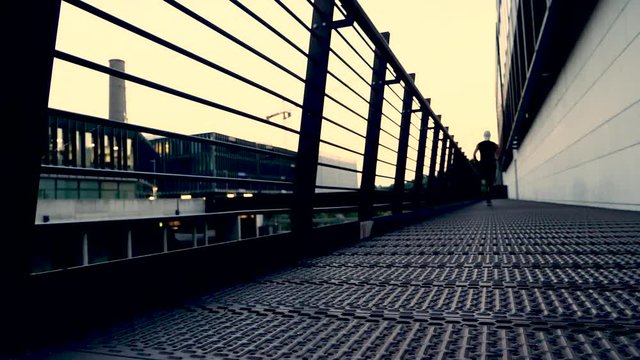 Attractive fit man running along modern bridge at sunset in slow motion
