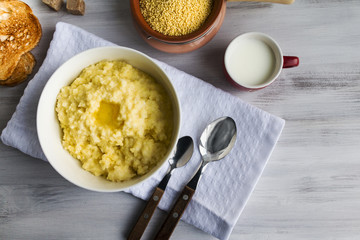 Wheat groats, millet porridge and melting butter in white bowl on kitchen table. Selective focus. Closeup. Copy space.