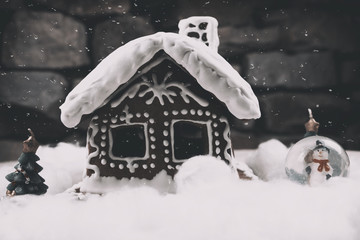 Naklejka premium Snowy Gingerbread house with snowflakes christmas tree and globe on stone wall background. Homemade christmas cookies - gingerbread on snow background. Closeup xmas gingerbread cottage in wintertime