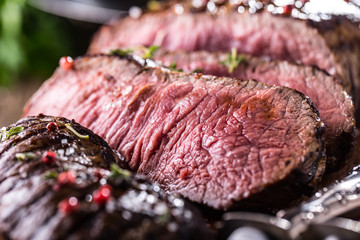 Beef steak. Juicy medium Rib Eye steak slices on wooden board with fork and knife herbs spices and salt