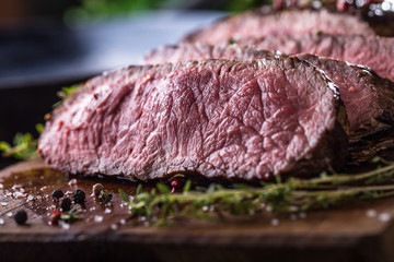 Beef steak. Juicy medium Rib Eye steak slices on wooden board with fork and knife herbs spices and salt
