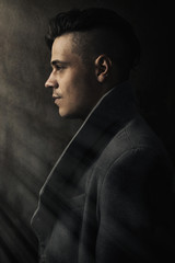 Vintrage retro Portrait of man from side with sunrays on dark background. Misty vintage portrait shot from profile with fog. Retro portrait in studio. Man illuminated  from side posing to camera.