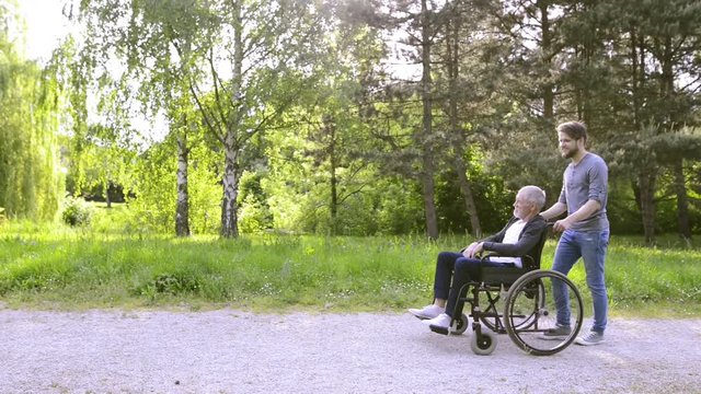 Son walking with disabled father in wheelchair outdoors.