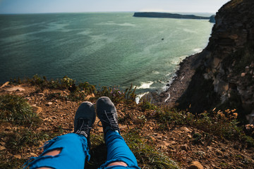 Plakat The legs of the girl in blue ragged jeans against the background of a stunning view from the rocks to the Japanese Sea
