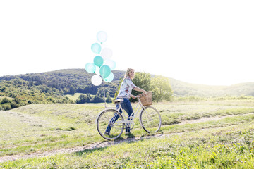 Obraz premium Happy Woman driving by bike with balloons