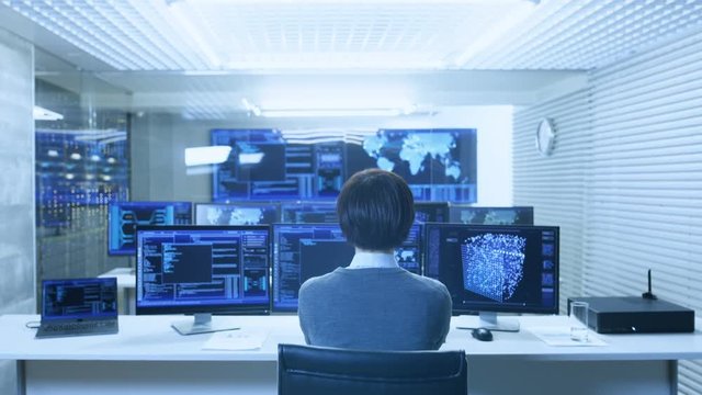 Back View of the IT Engineer Working with Multiple Monitors Showing Graphics, Functional Neural Network. He Works in a Technologically Advanced System Control Data Center.