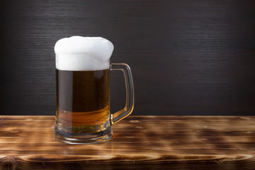 Mug of beer on wood surface. Dark background.