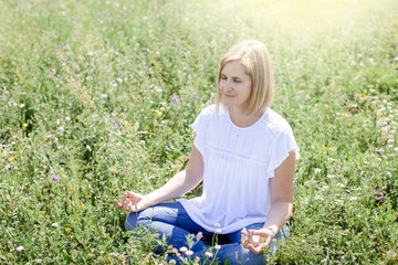 Happy woman is doing yoga in the meadow