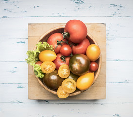 Colorful various of organic farm vegetables different varieties of tomatoes, fresh vegetables in a wooden bowl on a rustic background, top view