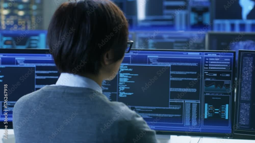 Poster In the System Control Room Technical Operator Stands and Monitors Various Activities Showing on Multiple Displays with Graphics.  Shot on RED EPIC-W 8K Helium Cinema Camera.