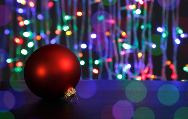 Red christmas ball on dark. Out of focus christmas lights background.