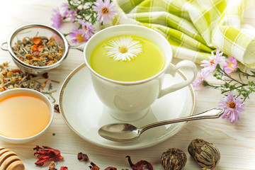 Green tea in a cup on a background of dry leaves of floral tea in a composition with accessories on a white background