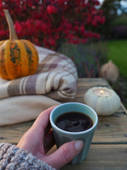 A woman holding a cup of coffe with the ornamental pumpkin, candle and blanket on backgroung.