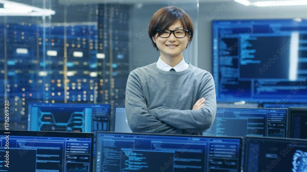 Poster In the System Control Room IT Technician Crosses Arms and Smiles. He's Surrounded by Multiple Displays Showing Graphics. 