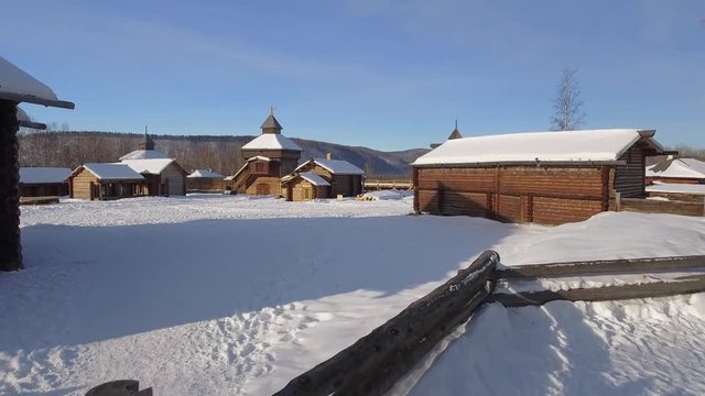 Old authentic Russian village Taltsy wooden Baikalsky tract buildings. Approach church domes roof snow Bikal. Tourist attraction. Winter frozen day. Aerial drone low gimbal cinematic 