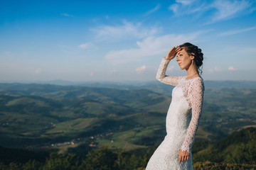 Bride looks far away standing on a green hill in a sunny day