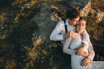 Cheerful newlyweds rest on the rocks in the rays of evening sun