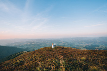 Look from afar at wedding standing on a hill with great landscape behind