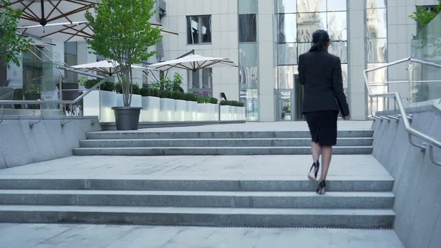 Businesswoman walking up the stairs to building, backside view, career ladder