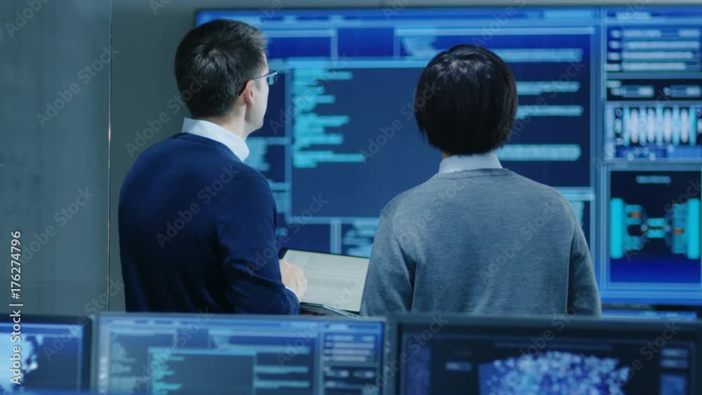 Aufkleber in the system control room it specialist and project engineer have discussion while holding laptop, 