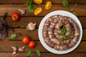 Raw fresh sausages in a white plate on a wooden background. Top view. Close-up