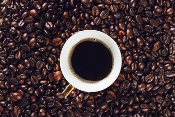 A cup of coffee on a background of roasted coffee beans
