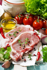 two pieces of pork on a cutting board and fresh foods, vertical