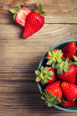 Strawberries in a green bowl and halved strawberry on a wooden table