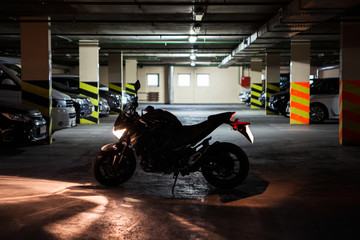 Silhouette of running engine motorcycle standing in the mile of dark underground parking. Light is...
