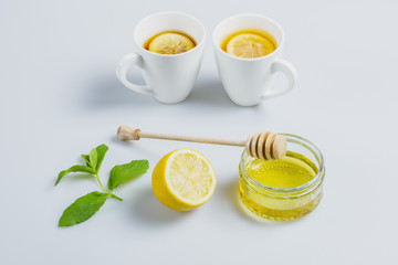 Two cups of black tea, lemon, mint and honey on a white kitchen table