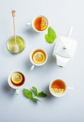 Four cups of tea, kettle and honey on a white table, top view