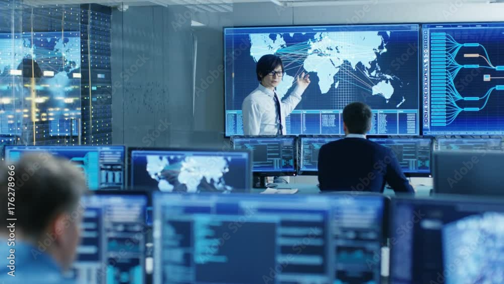 Poster In the System Control Room Manager Holds a Briefing for His Staff Members. They're Work in Data Center and are Surrounded by Multiple Screens Showing Maps, Logistics Data. 