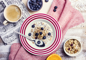 Tasty muesli with milk, blueberries and cranberrues and a cup of coffee on a white wooden table