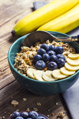 Muesli with blueberries and banana in a green bowl on a wooden table