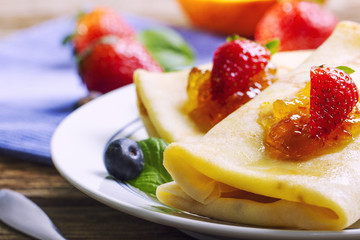 Tasty crepes with jam, strawberries and blueberries on a wooden kitchen table