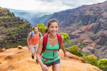 Hiking people on Hawaii Waimea Canyon Trail, Kauai island, USA. Young woman and man hikers walking in mountain nature landscape in mountains. Asian girl hiker in foreground.