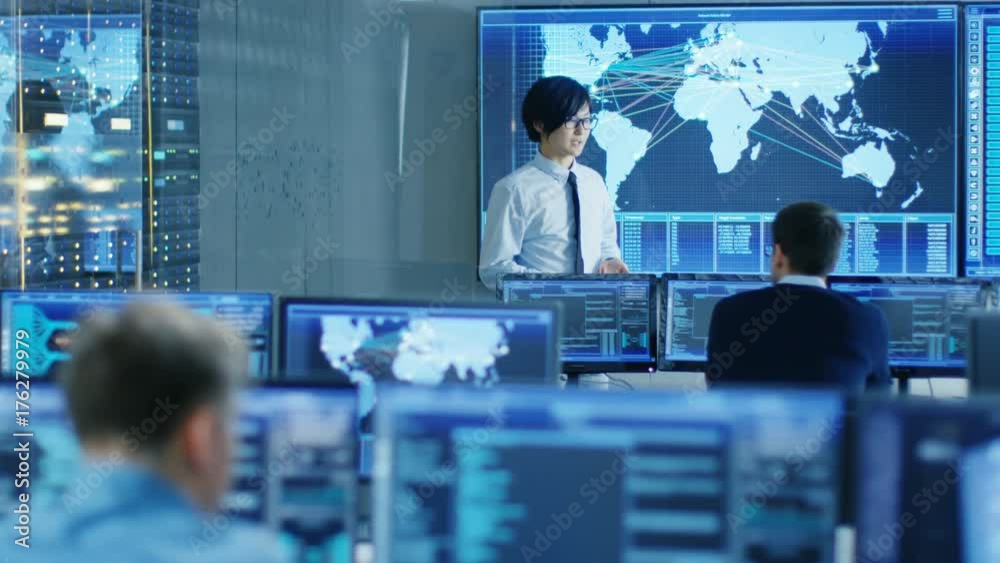 Poster In the System Control Room Manager Holds a Briefing for His Staff Members. They're Work in Data Center and are Surrounded by Multiple Screens Showing Maps, Logistics Data. 