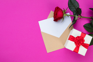 Romantic vintage pink background of a blank card with envelope, red rose and gift wrap with a red bow. Copy space, view from above