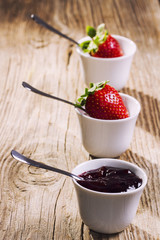 Strawberry jam and fresh strawberries in mini bowls on wooden table