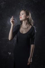 Fototapeta premium Girl in a reverie mood. Noir film style woman in dress holding black pen in her hand. Studio shot. Old fashion photo