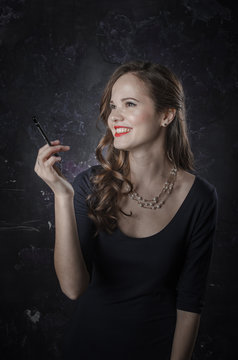 Female in a good mood and smiling. Noir film style woman in dress holding black pen. Studio shot. Old fashion photo