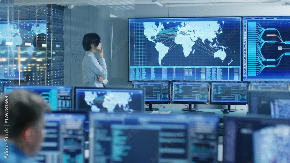 Poster In the System Control Room Chief Engineer Thinks While Standing Before Big Screen with Interactive Map on it. Data Center is Full of Monitors Showing Graphics. 