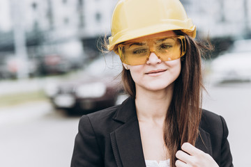 Close up portrait of beautiful girl in a yellow protective helmet and protective glasses, an architectural concept