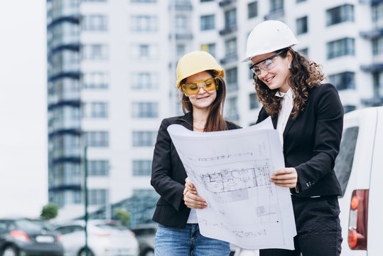 Two business women in protective helmets and safety glasses looking at building schemes, architectural concept