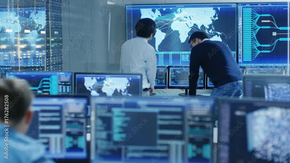 Fototapete In the System Control Room Project Manage and IT Engineer Have Discussion, they're surrounded by Multiple Monitors with Graphics. Big Monitor Shows Interactive Logistics Map. 