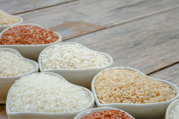 Jasmine rice and different rice in ceramic bowl on old plank
