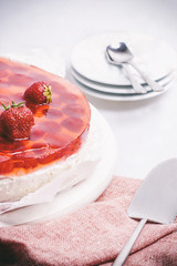 Cheesecake with strawberries, plates and pink kitchen towel on white table