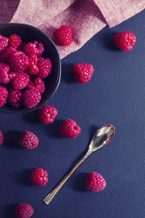 Fresh raspberries in a bowl and a golden spoon on black table, view from top