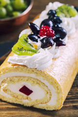 Homemade roll cake decorated with fresh fruits on wooden table,