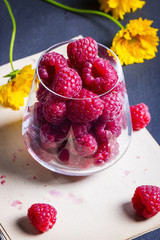 Ripe raspberries in glass and yellow flowers on stone kitchen table